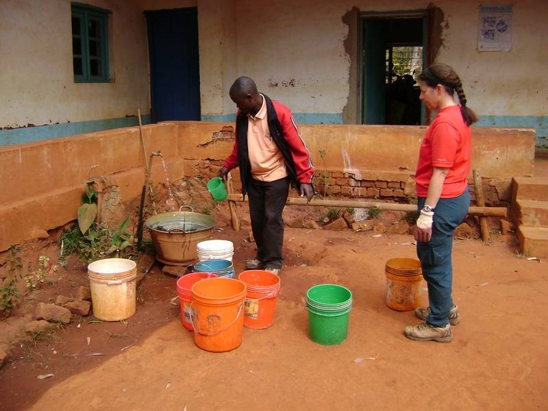 Carrying water in buckets from the Clinic to refill a small water tank on site to mix concrete
